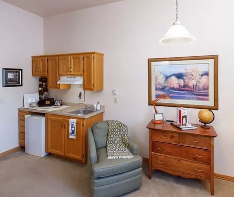 A well-furnished kitchenette with a living area featuring a chair and decorative items.