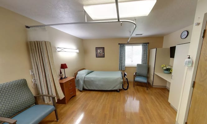 Private bedroom with a bed, chair, and dresser in a senior living facility.