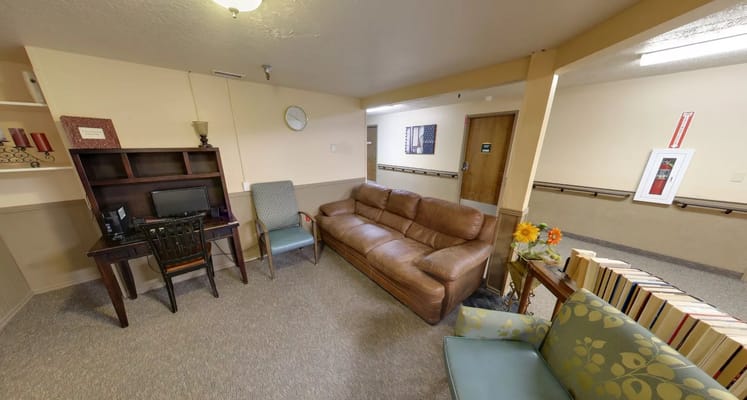 A cozy living room with a brown couch, blue armchair, and a desk with a computer