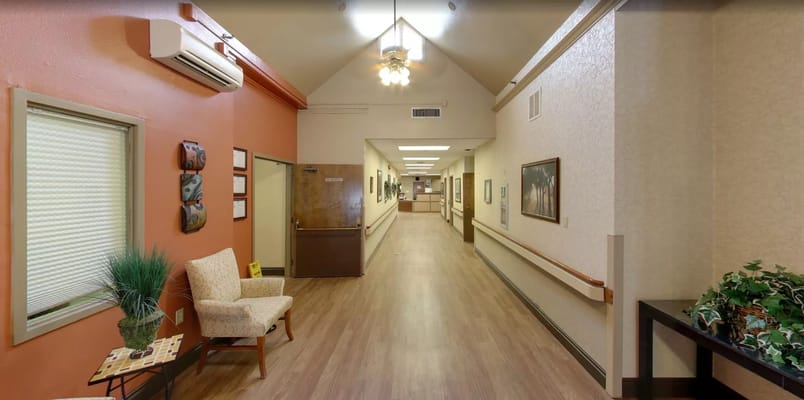 A well-lit hallway with beige walls and wooden flooring, featuring a chair and decorative elements.