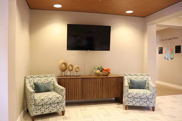 A cozy lobby featuring two patterned chairs and a wooden side table with decorative items.