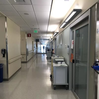 A brightly lit hallway in a healthcare facility with medical carts and rooms on either side.