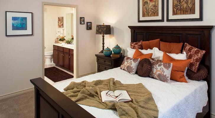 A cozy bedroom featuring a bed with decorative pillows and a view into a bathroom.