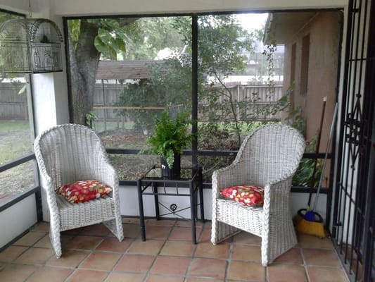 Two wicker chairs with colorful cushions on a screened porch.