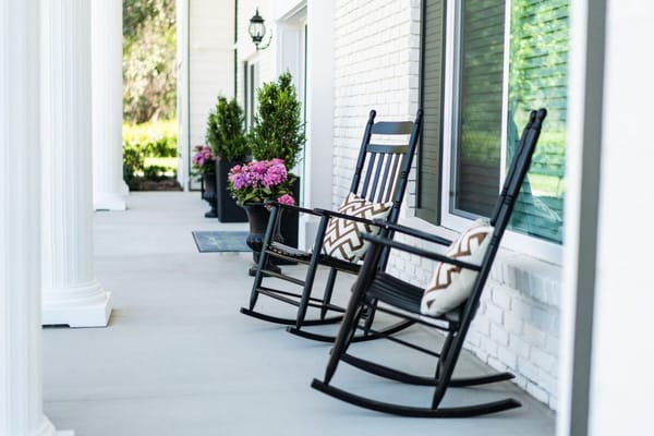 Two black rocking chairs with cushions on a porch overlooking potted plants.