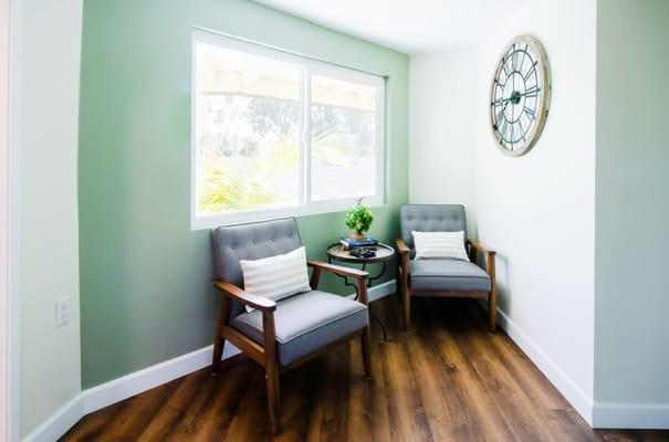 A cozy lounge area with two grey chairs and a clock on the wall.