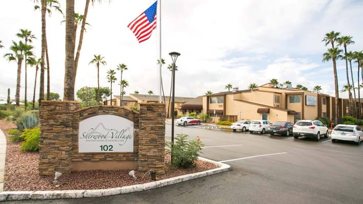 Entrance sign of Sherwood Village with palm trees and American flag