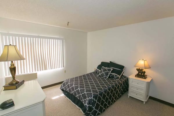 A well-lit bedroom with a bed and bedside table in Sherwood Village.