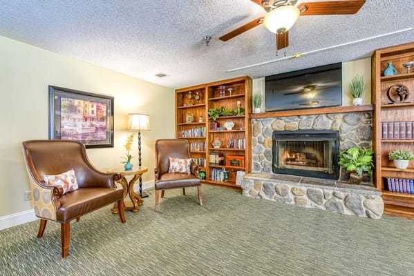 A spacious living room with two chairs, a lamp, and a stone fireplace.