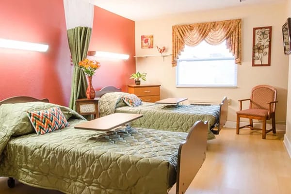 A shared bedroom with two green beds and a chair, decorated with curtains and floral accents.