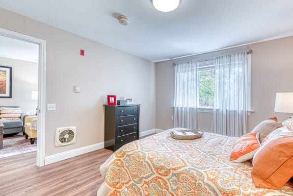 A cozy bedroom with an orange patterned bedspread, dresser, and window