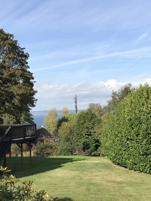 A scenic view of a garden with trees, shrubs, and a glimpse of the water in the background.