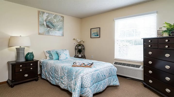 A cozy bedroom featuring a bed with blue and white bedding, a nightstand, and a dresser.