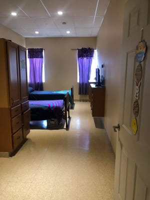 Interior view of a shared bedroom with two beds and purple curtains