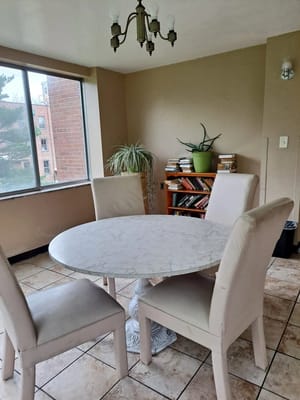 A round marble dining table surrounded by four beige chairs in a well-lit room.