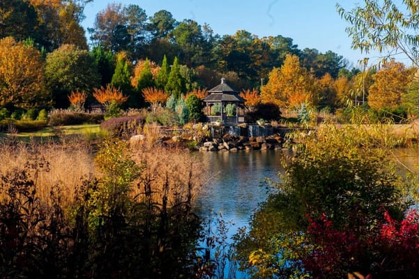 A gazebo surrounded by colorful trees and a tranquil pond.