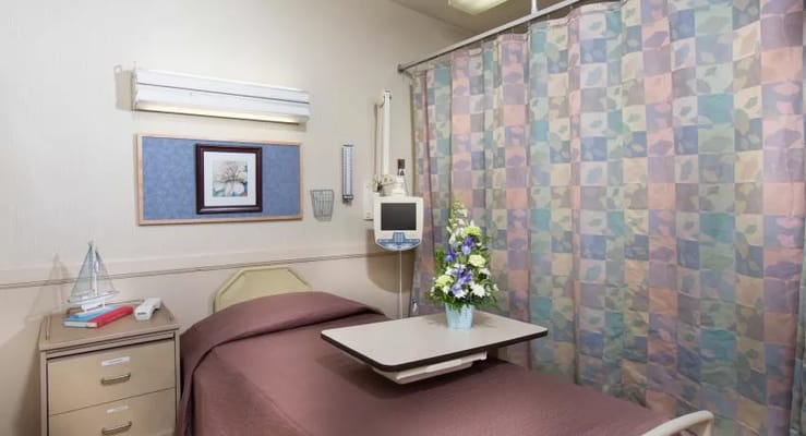 A cozy patient room featuring a bed, bedside table, and a decorative curtain.