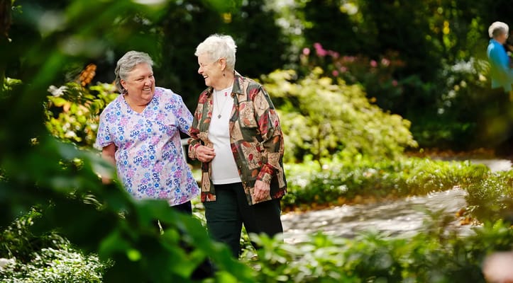 Two women walking together in a lush garden