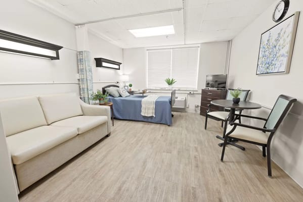A well-furnished bedroom in St. Joseph's Assisted Living facility, featuring a bed, sofa, and small dining table.