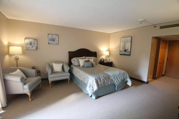 A cozy bedroom with a bed, armchairs, and decorative artwork.