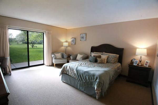 Spacious bedroom with a bed, chair, lamp, and sliding glass door to outside.