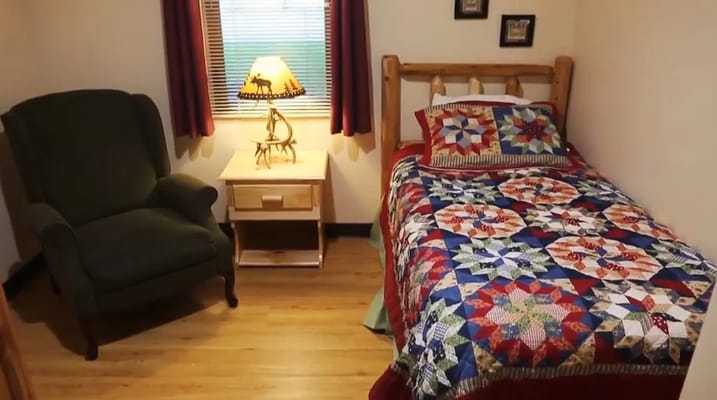 A cozy bedroom with a colorful quilt and armchair.