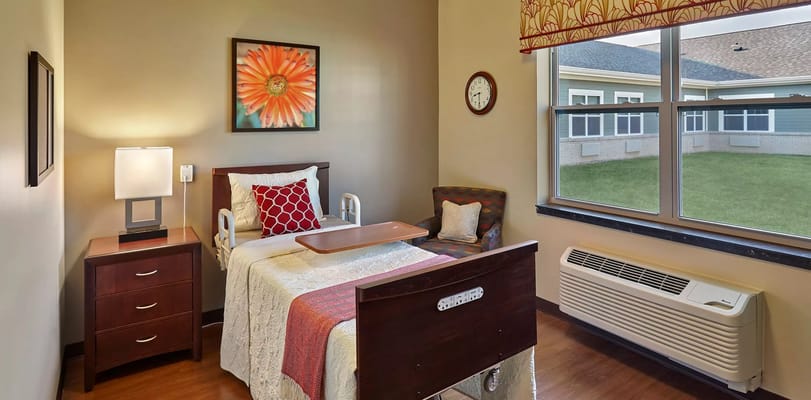 A well-furnished bedroom featuring a hospital bed, bedside table, and a decorative chair.
