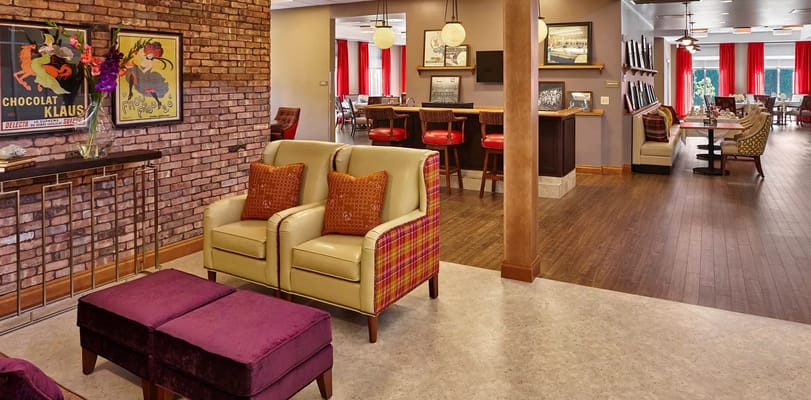 Lounge area with yellow chairs, purple ottoman, and exposed brick wall.