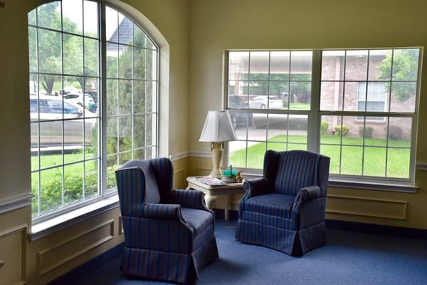 Two blue striped chairs next to a lamp and table with a window view.