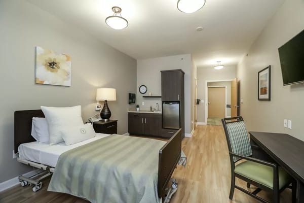 A spacious and well-furnished resident room with a bed, kitchenette, and desk.