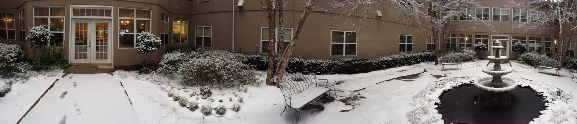 Snow-covered patio with a fountain and greenery.