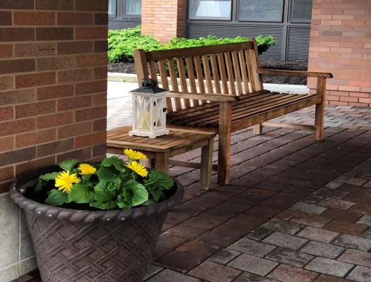 Wooden bench with yellow flowers in a pot beside a lantern.