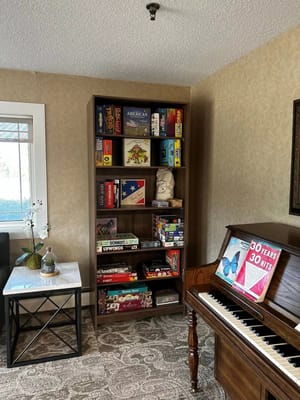 A common area featuring a bookshelf filled with board games and a piano.