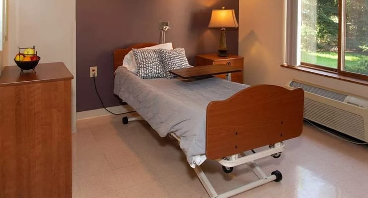 A well-appointed bedroom in a senior living facility with a bed, nightstand, and window.