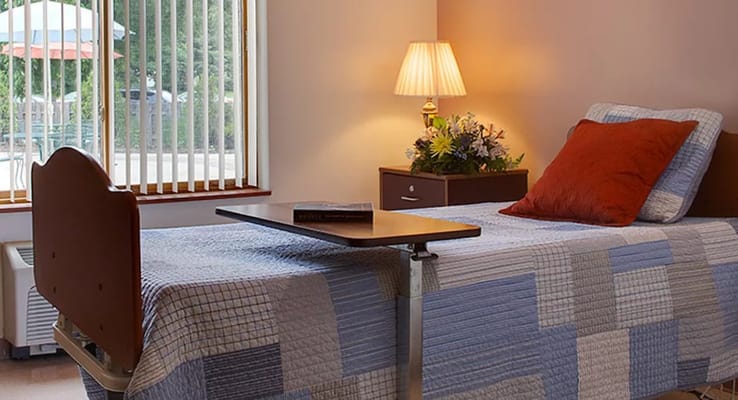 A cozy bedroom with a bed, lamp, and flowers.