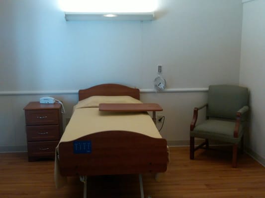 A private room with a hospital bed, nightstand, and armchair.