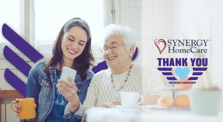 Caregiver and senior woman smiling while looking at a phone