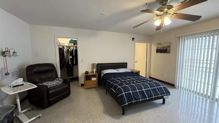 A cozy bedroom with a bed and recliner in Tender Loving Memory Care.