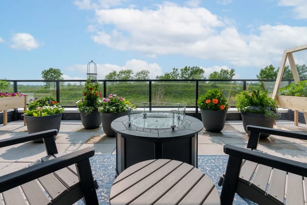 A rooftop garden patio with vibrant flowers and a central fire pit.
