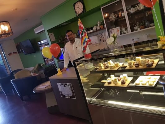 A staff member stands behind a café counter with sweets and decorations.