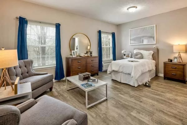 A well-furnished bedroom in a senior living facility, featuring a bed, dresser, and seating area.