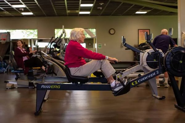 Senior woman rowing on an exercise machine at a health care center.