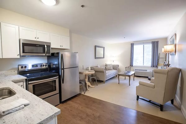 Cozy living room featuring a sofa, armchair, and kitchen appliances