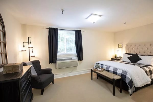 A well-furnished bedroom with a bed, armchair, and dresser.