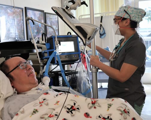 Health care professional attending to a patient in bed with medical equipment.