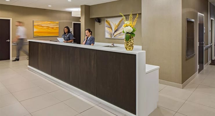Two staff members at the reception desk with flowers in a vase.