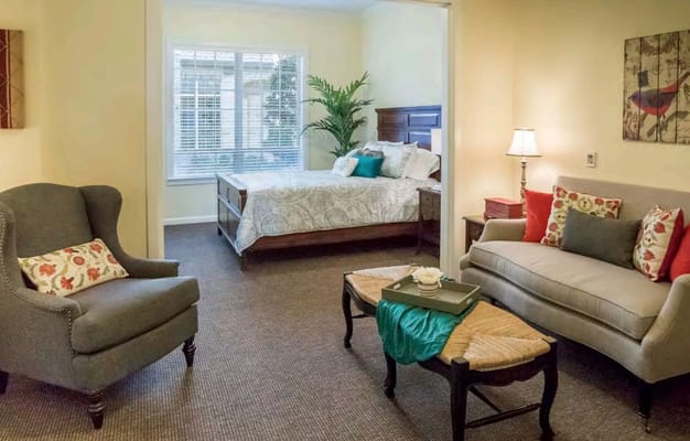 A comfortable bedroom and living area featuring a bed, armchair, and decorative sofa