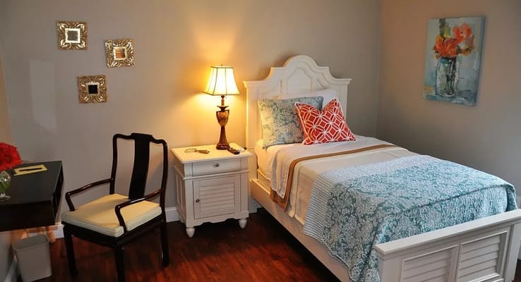 A cozy bedroom featuring a bed with decorative pillows, a lamp, and a chair.