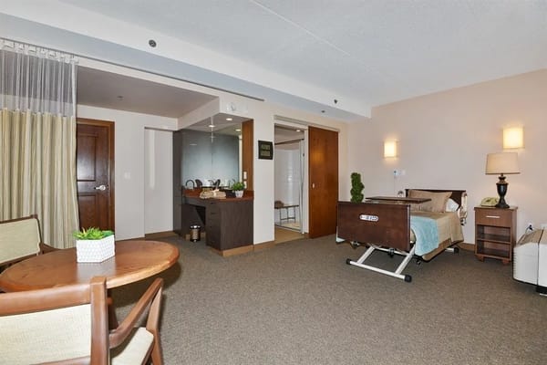 A well-furnished resident room with a bed, table, and bathroom entrance.