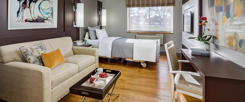 Cozy living area with a sofa, bed, and desk in a senior living facility room